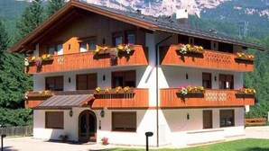 A two-story building with balconies, a front entrance, and a mountain backdrop. - Chalet Stadio (Cortina d'Ampezzo)
