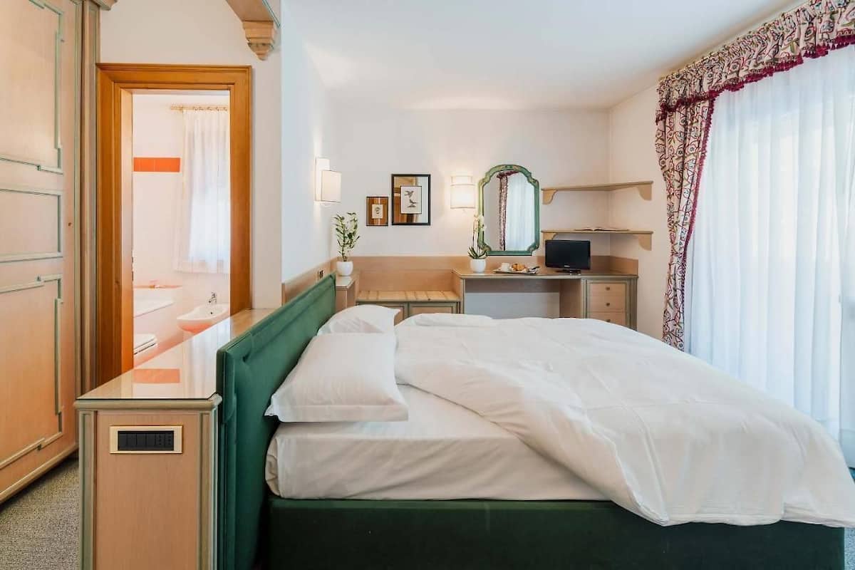 Ein Hotelzimmer mit Bett, Schreibtisch, Spiegel und Fernseher.