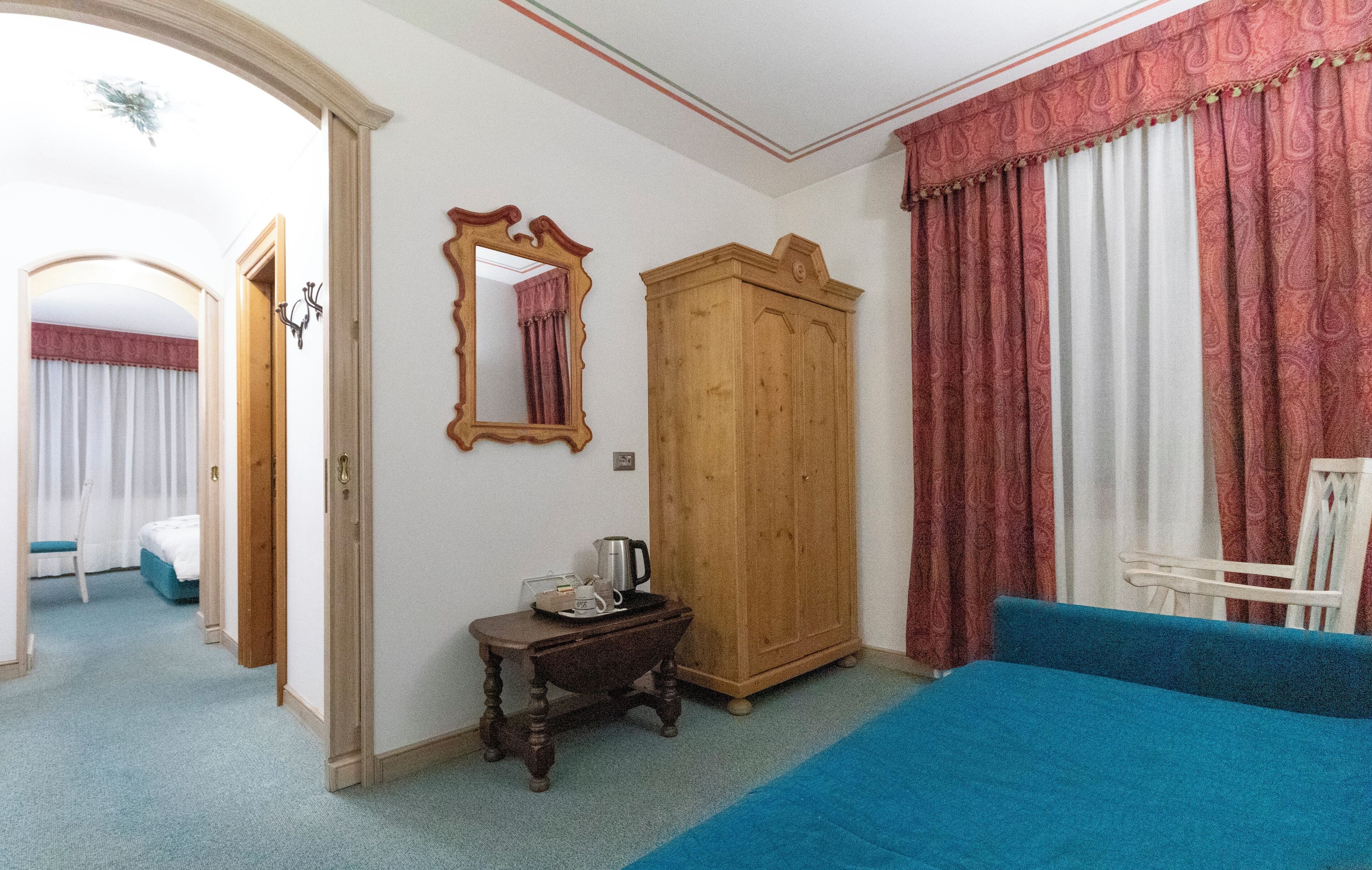 Quarto com cama azul, guarda-roupa de madeira, uma mesinha com chaleira e espelho na parede.