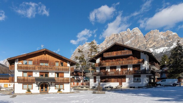 A snow-covered building with wooden balconies and a mountain backdrop. - Chalet Stadio (Cortina d'Ampezzo)