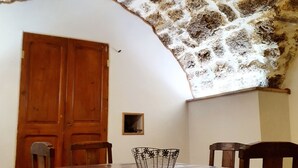 A dining area with a wooden table and chairs, a decorative metal basket, and a stone wall. - Fully renovated 2 to 3 person gîte (Saint-Rome-de-Tarn)