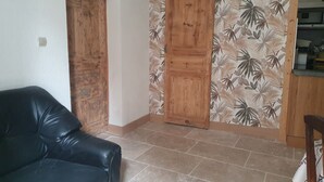 A room with a black leather sofa, a wooden door, and a wall with a tropical leaf pattern. - Fully renovated 2 to 3 person gîte (Saint-Rome-de-Tarn)