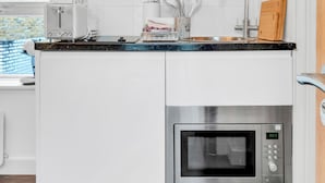 Une cuisine moderne avec des armoires blanches, un four à micro-ondes en acier inoxydable, un four encastré, un téléviseur à écran plat et une fenêtre donnant sur un mur en briques.