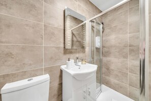 A modern bathroom with beige tiles, a white sink, a glass shower enclosure, and a toilet. - Sleek Studio Nest: Comfort in City Center (London)