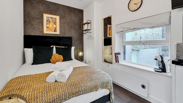 Une chambre d’hôtel moderne avec un grand lit, une horloge murale, une fenêtre donnant sur un beau paysage et une machine à café posée sur le rebord de la fenêtre.