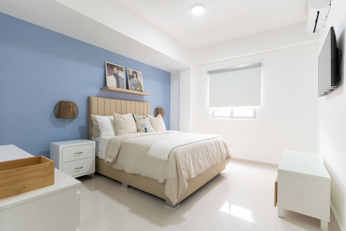 Un dormitorio moderno con cama, mesitas de noche, televisor y ventana.