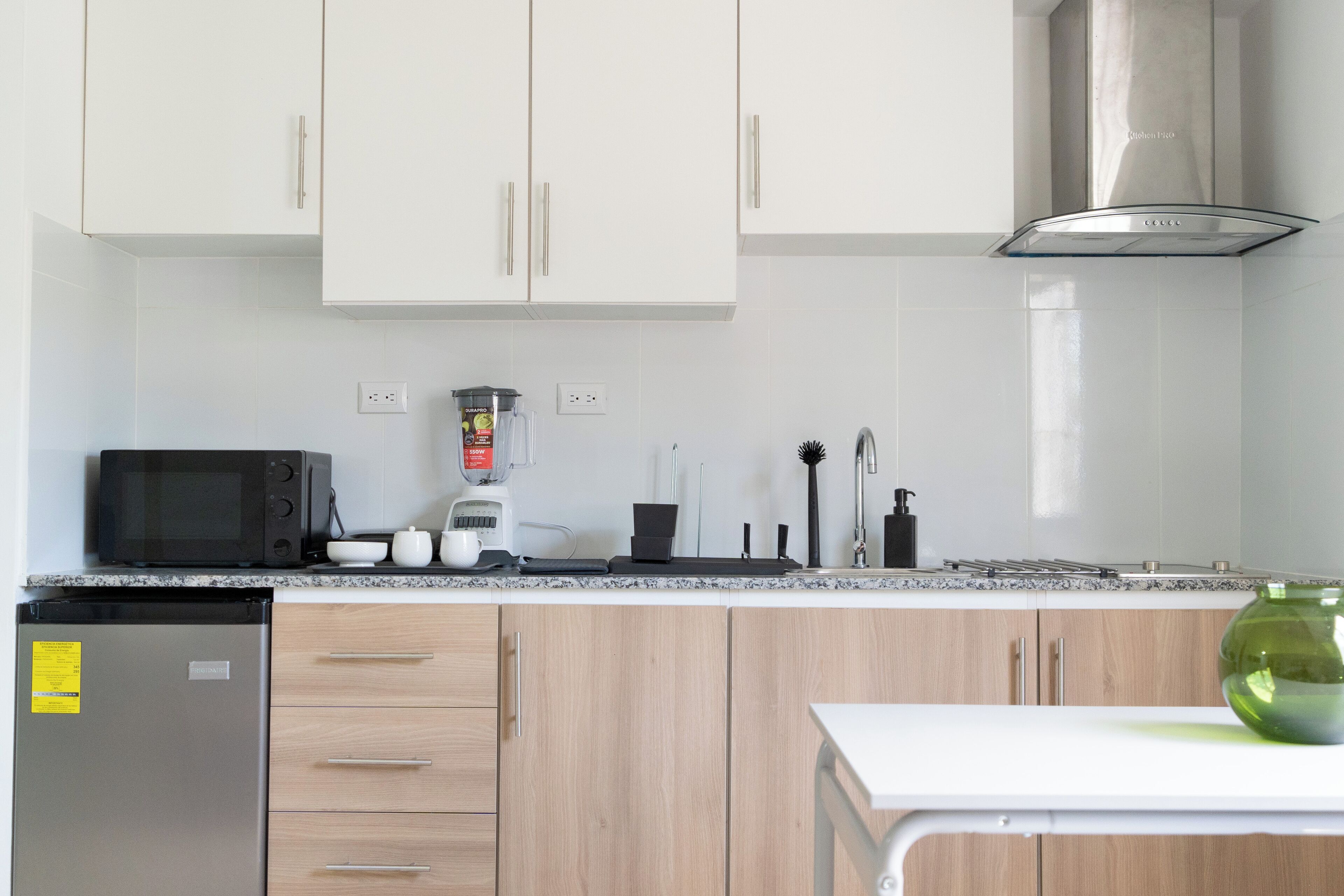 A modern kitchen with white cabinets, a microwave, a blender, and a sink.