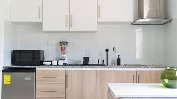 A modern kitchen with white cabinets, a microwave, a blender, and a sink.