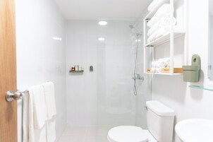 Un baño moderno con cabina de ducha de vidrio, sanitarios blancos y toallas ordenadas.