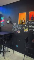 Una zona de bar con un letrero de neón, un cactus, una botella de licor y una pared con texto y dibujos.