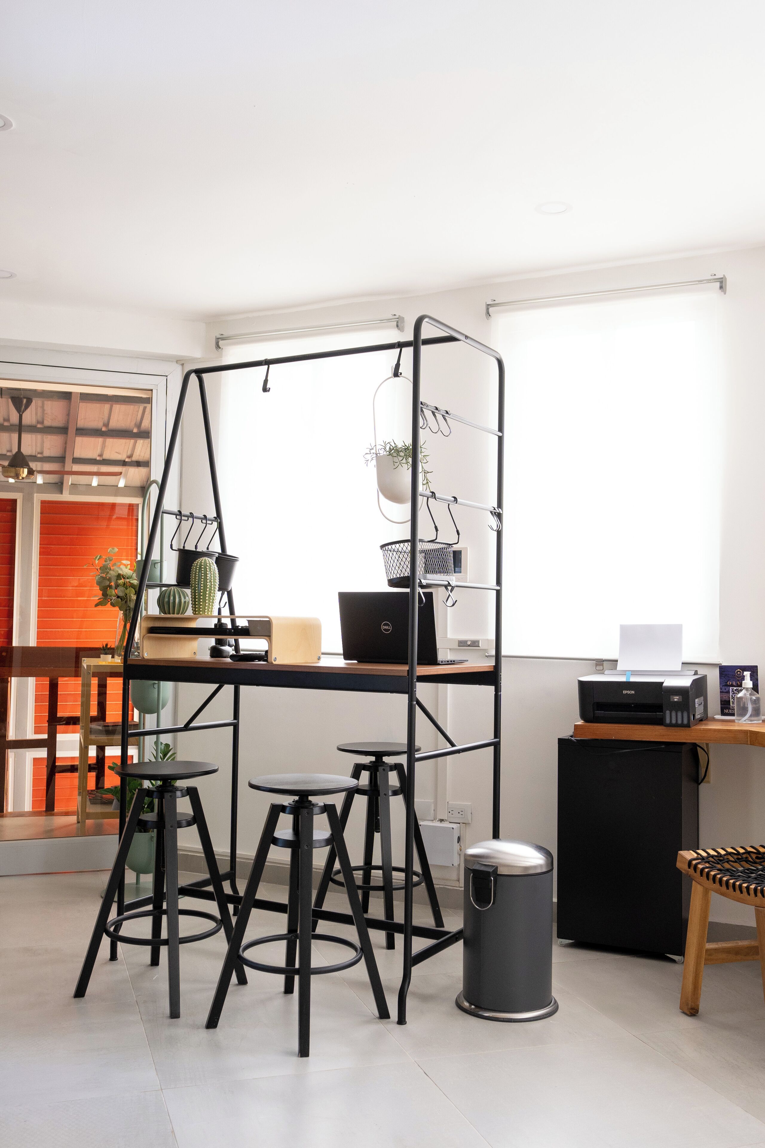 Un espacio de trabajo moderno con un escritorio metálico, taburetes y un cubo de basura.