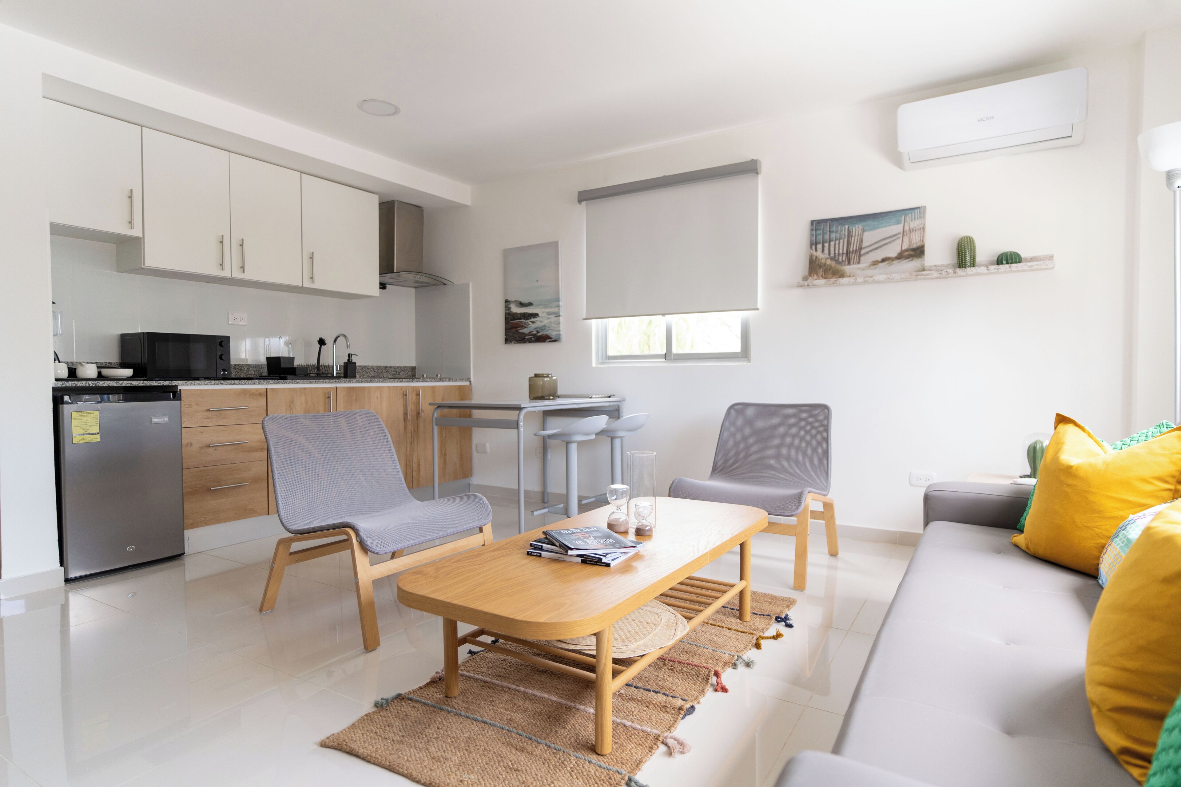 Een moderne woonkamer met een bank, twee stoelen, een salontafel en een keukenhoek met kasten en apparatuur.