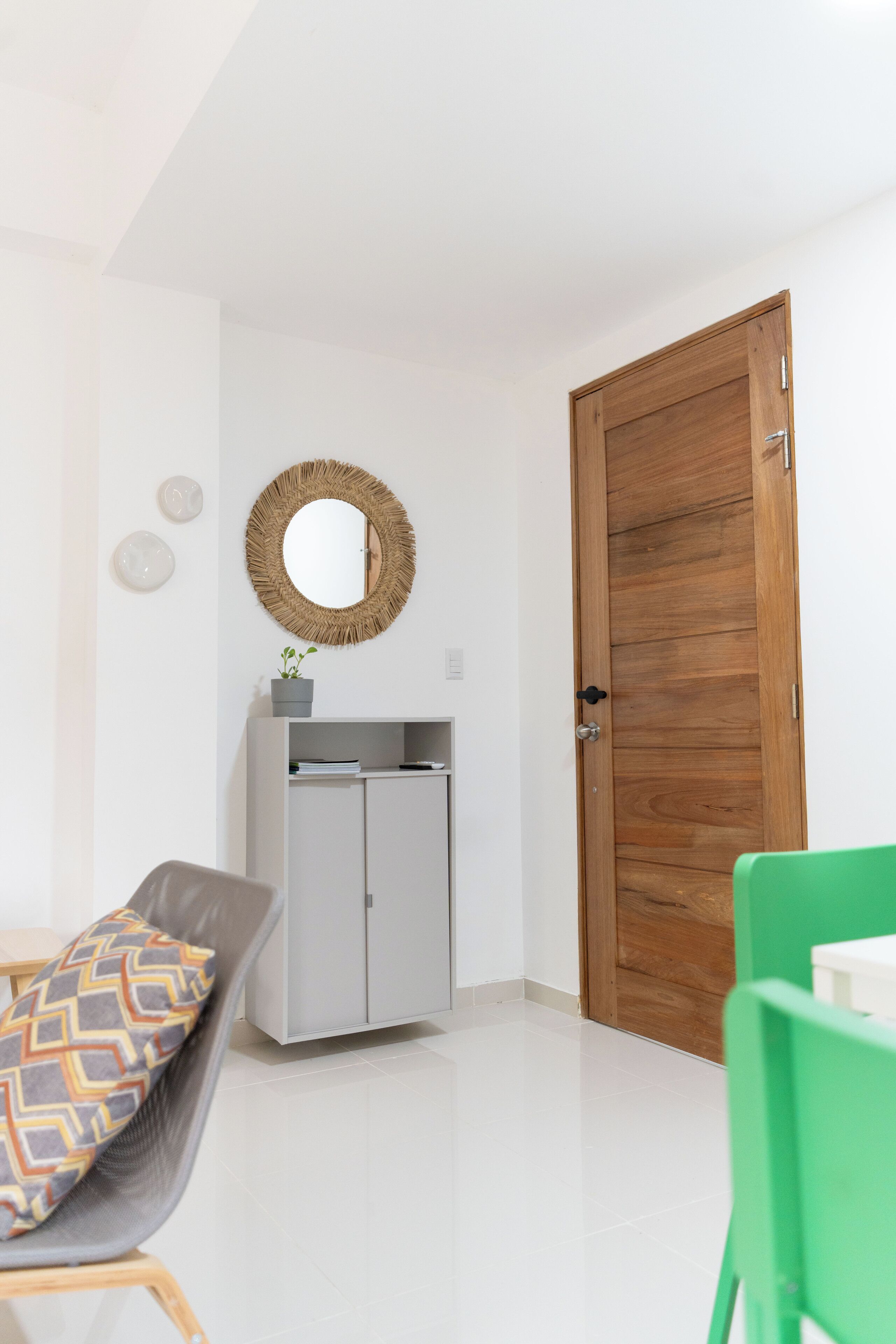 Une chambre moderne avec une porte en bois, un meuble gris doté d’un miroir et une chaise verte.