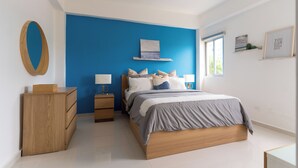 A bedroom with a bed, wooden dresser, bedside tables, and a blue accent wall. - Landa Mar Boca Chica (Boca Chica)