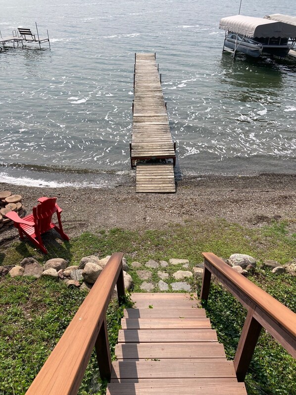 A wooden dock leading to a body of water with a rowboat and a covered pontoon. - Charming 2-bedroom cabin on Keuka Lake close to Penn Yan & the Keuka Wine Trail (Penn Yan)