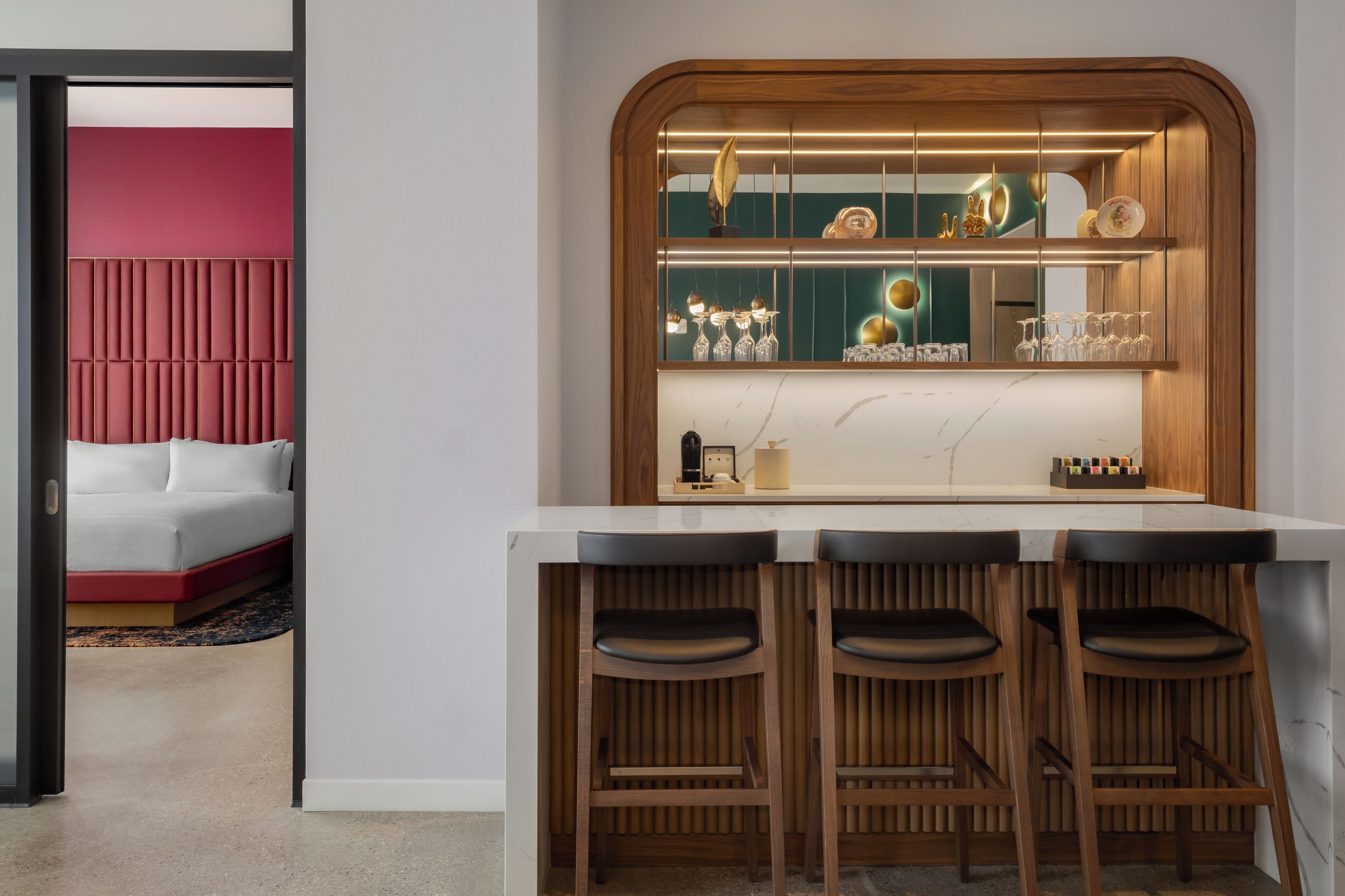 A modern kitchen with a bar area, wooden stools, and a red accent wall.
