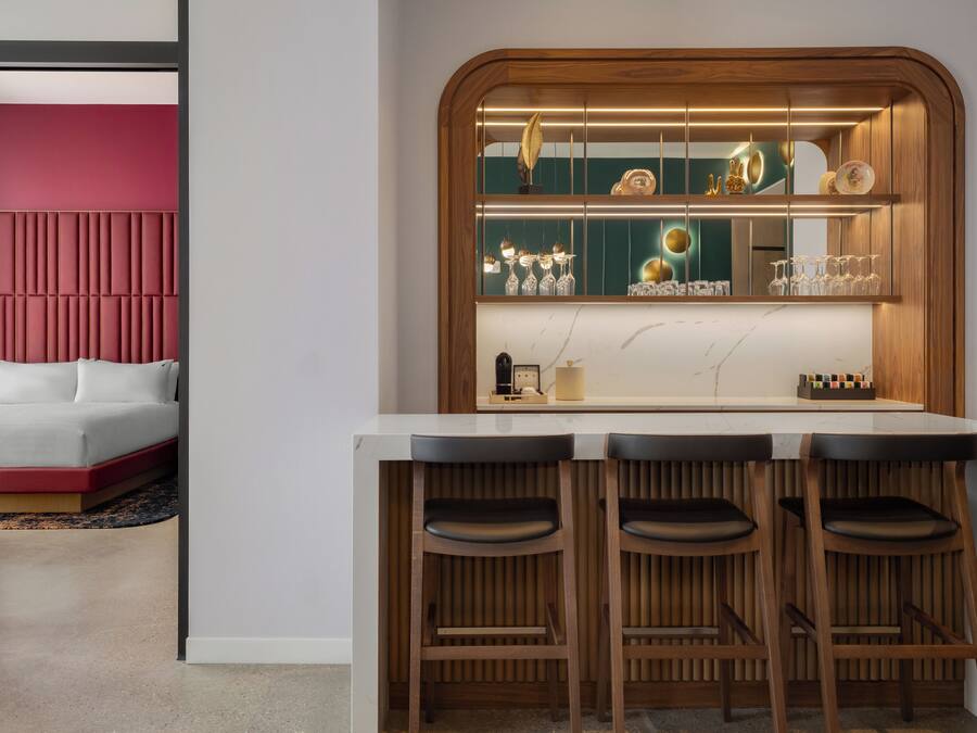 A modern kitchen with a bar area, wooden stools, and a red accent wall.