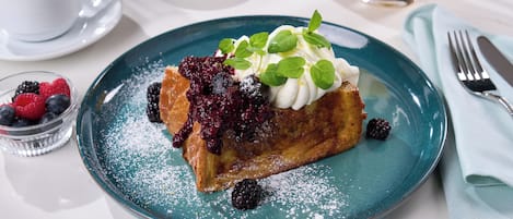 A dessert plate with a slice of cake, berries, and whipped cream on a teal plate.