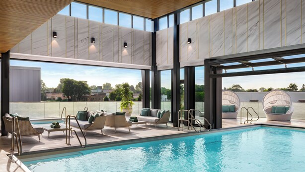 Un área de piscina interior moderna con sillones de descanso y vistas al exterior.