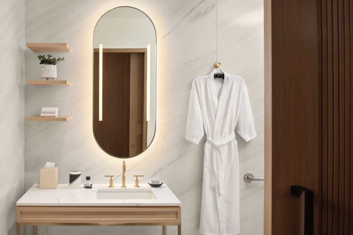 Une salle de bain moderne avec un lavabo en marbre, un grand miroir et un peignoir accroché à la porte.
