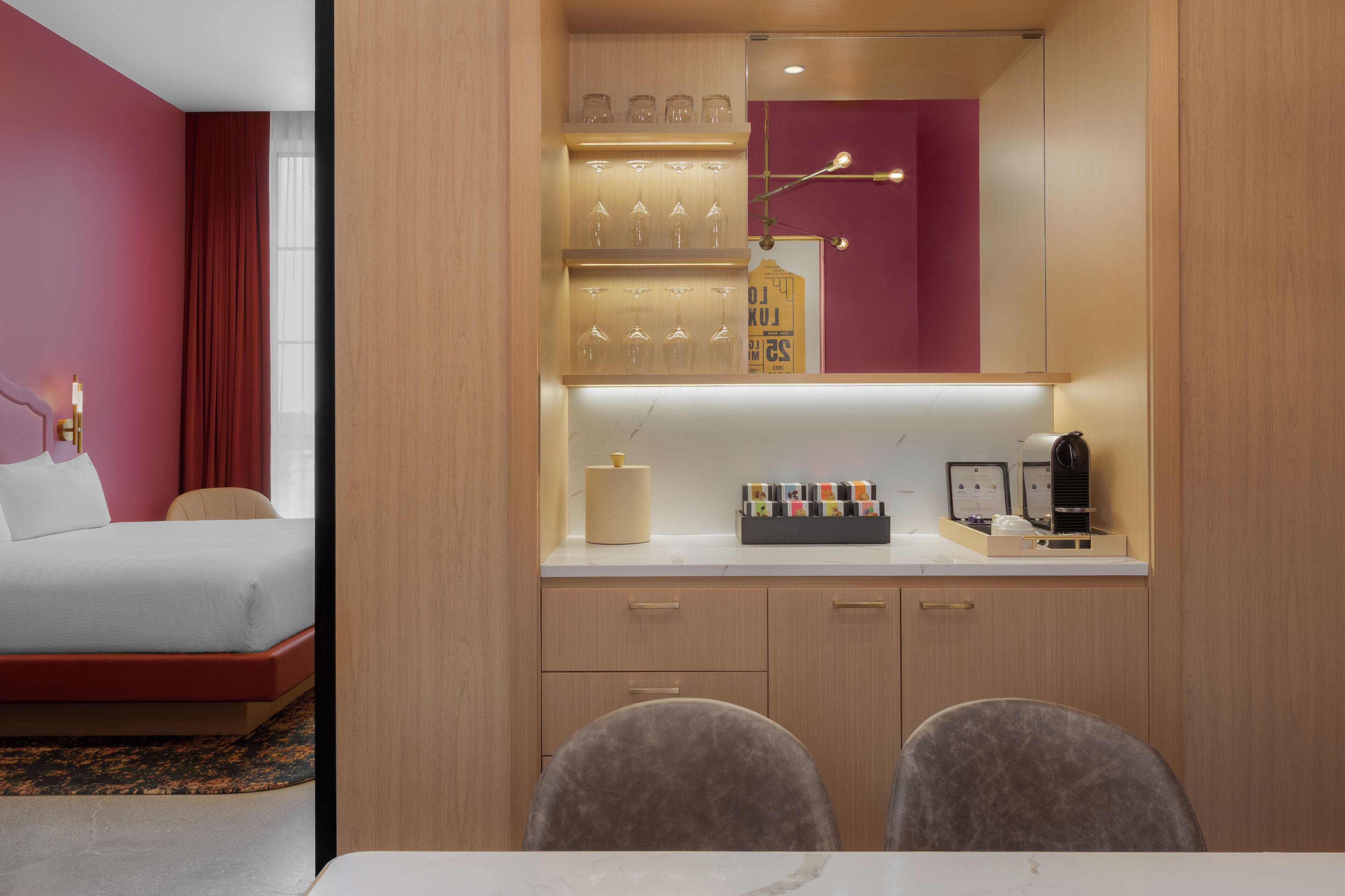A hotel room with a bed, a desk with a chair, a minibar, and a mirror.