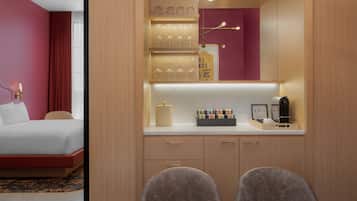 A hotel room with a bed, a desk with a chair, a minibar, and a mirror.