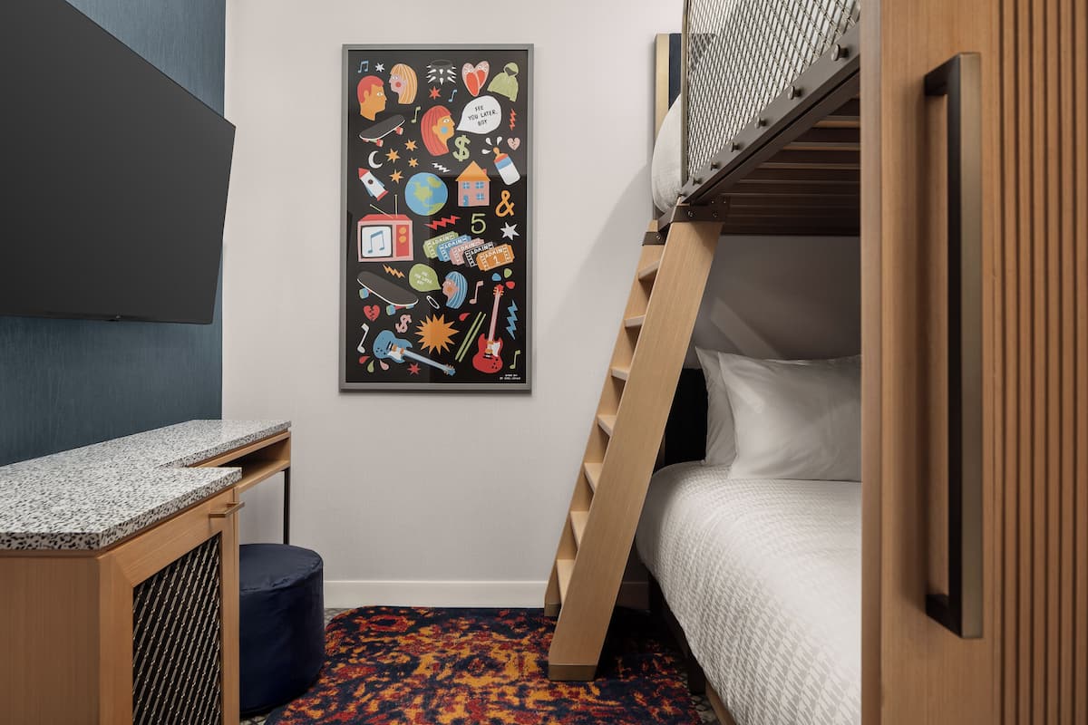 Une chambre avec des lits superposés, un bureau, une affiche abstraite aux couleurs vives accrochée au mur et un tapis à motifs.