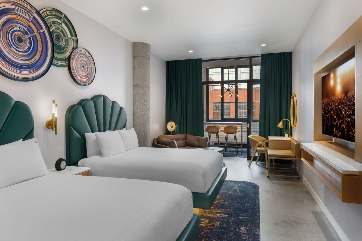 Habitación de hotel con dos camas, un área de descanso, un ventanal grande y vistas a la ciudad.