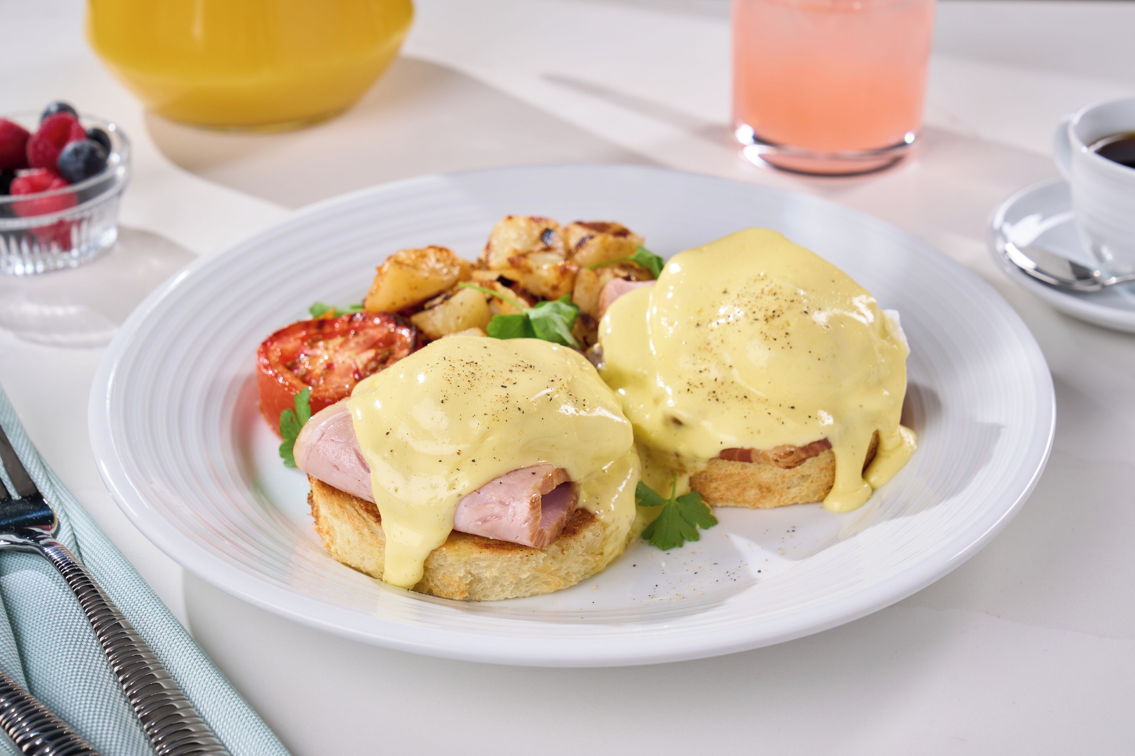 A breakfast plate with eggs benedict, hash browns, and a side of fruit.