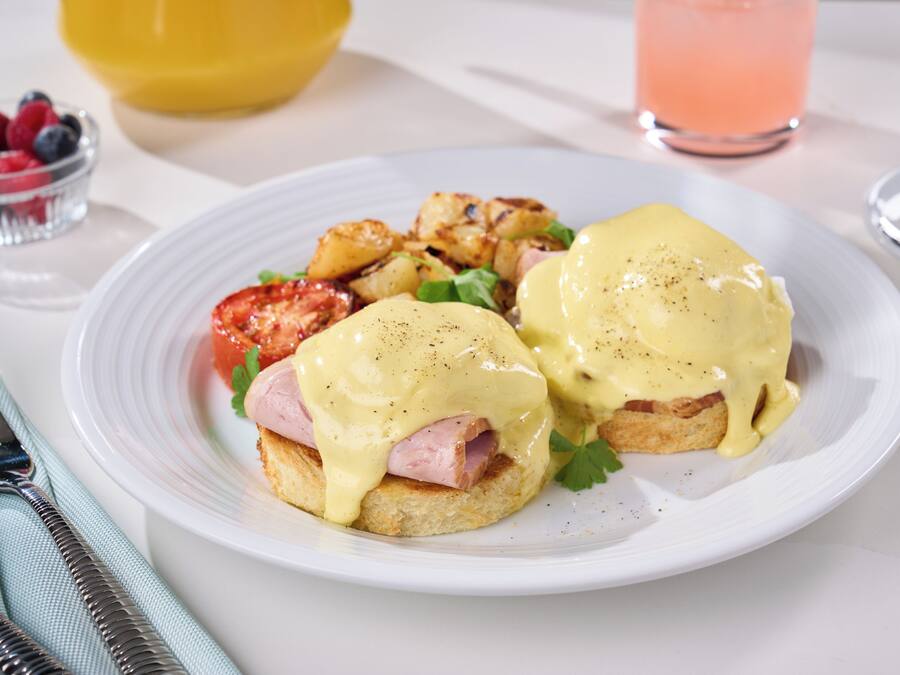 Aamiainen, joka sisältää munia Benedict-kastikkeessa, perunaraastetta ja hedelmiä.