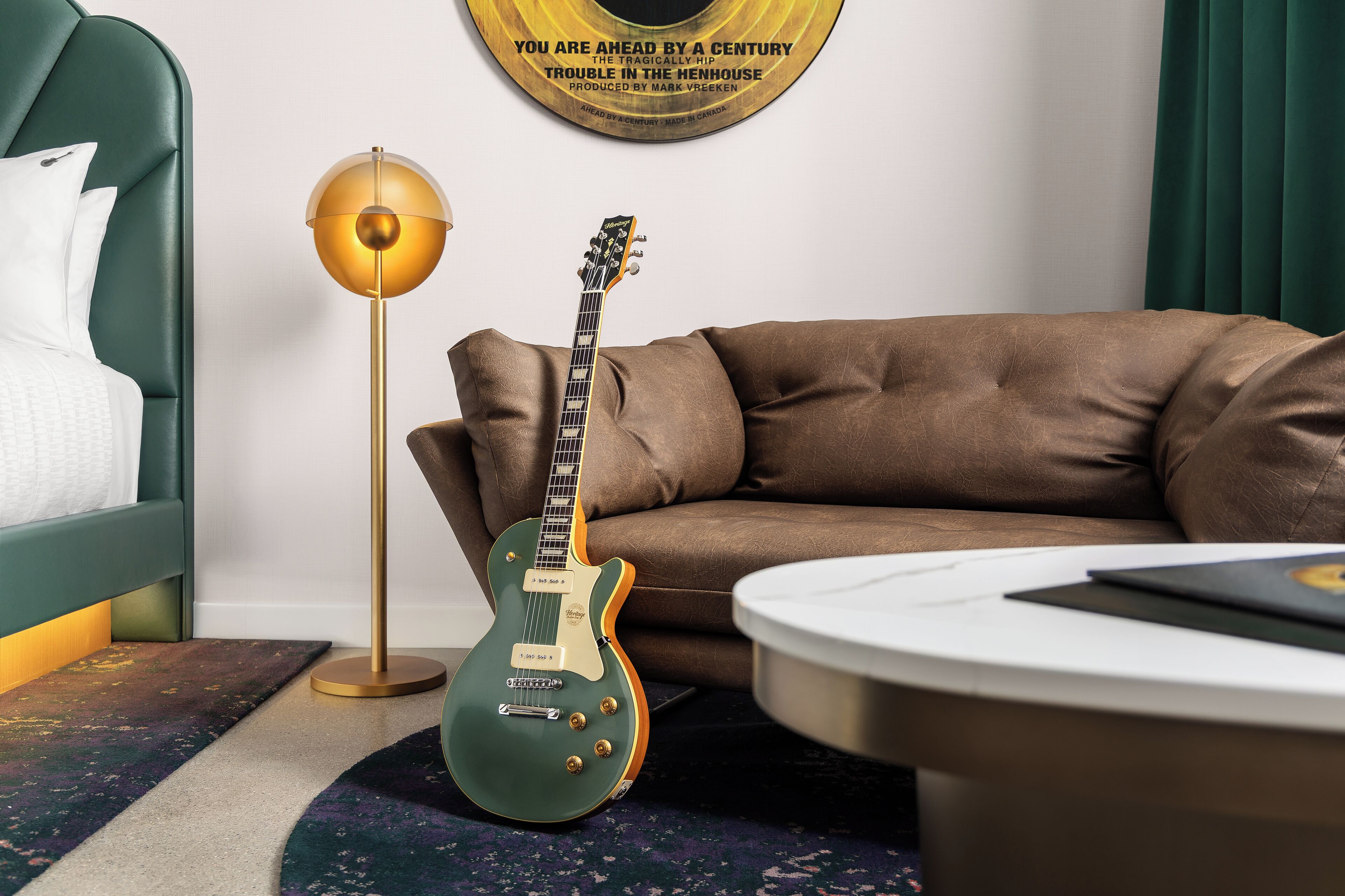 Una habitación con un sofá tapizado en verde, una guitarra eléctrica verde, una lámpara de pie y un tocadiscos montado en la pared.