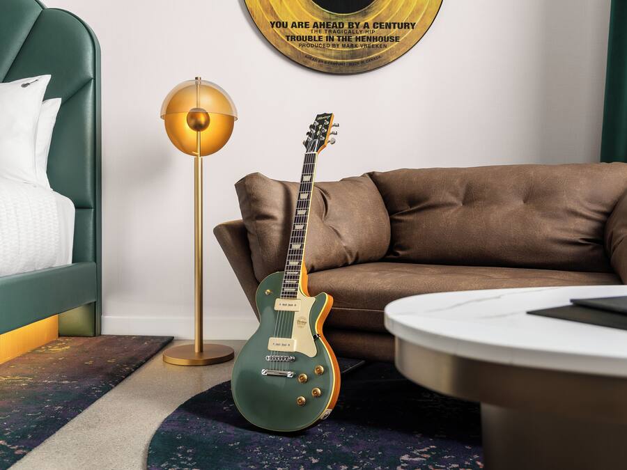 Una habitación con un sofá tapizado en verde, una guitarra eléctrica verde, una lámpara de pie y un tocadiscos montado en la pared.