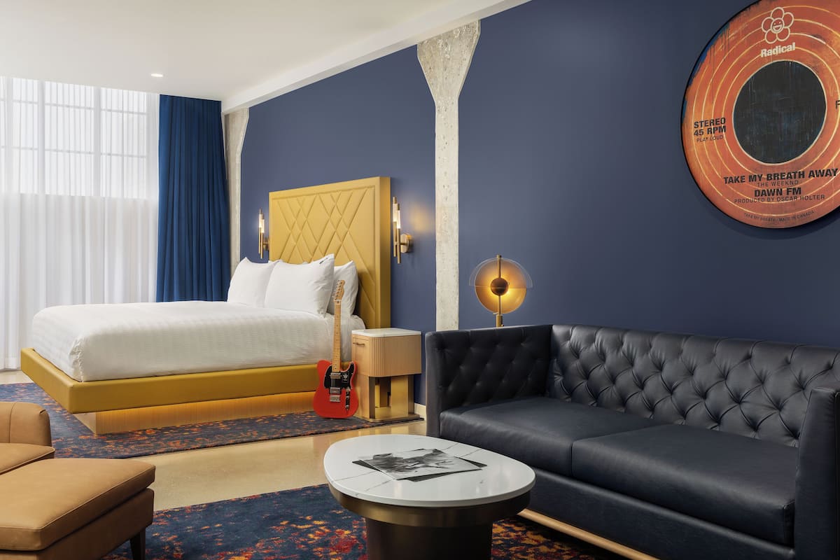 Une chambre d’hôtel avec un lit, un canapé, une table basse et un mur décoré d’une pochette de disque.