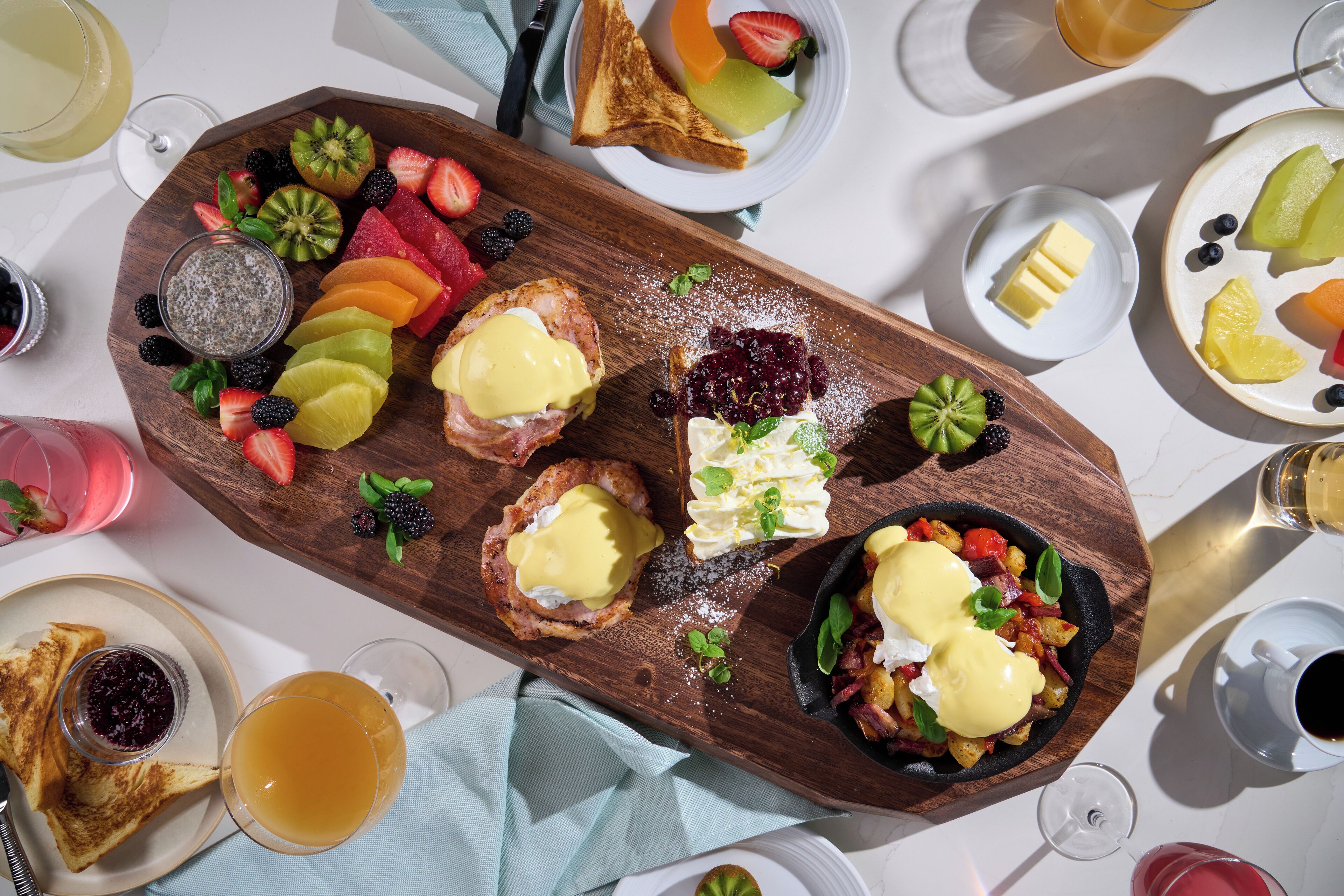 Ein reichhaltiges Frühstücksbuffet mit Toast, Obst und Eiern auf einer Holzplatte.