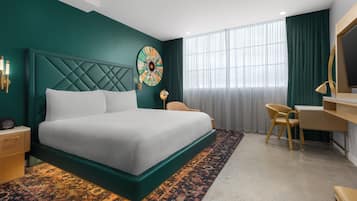 Ett modernt hotellrum med en stor säng, ett skrivbord, en stol och ett stort fönster med gardiner.
