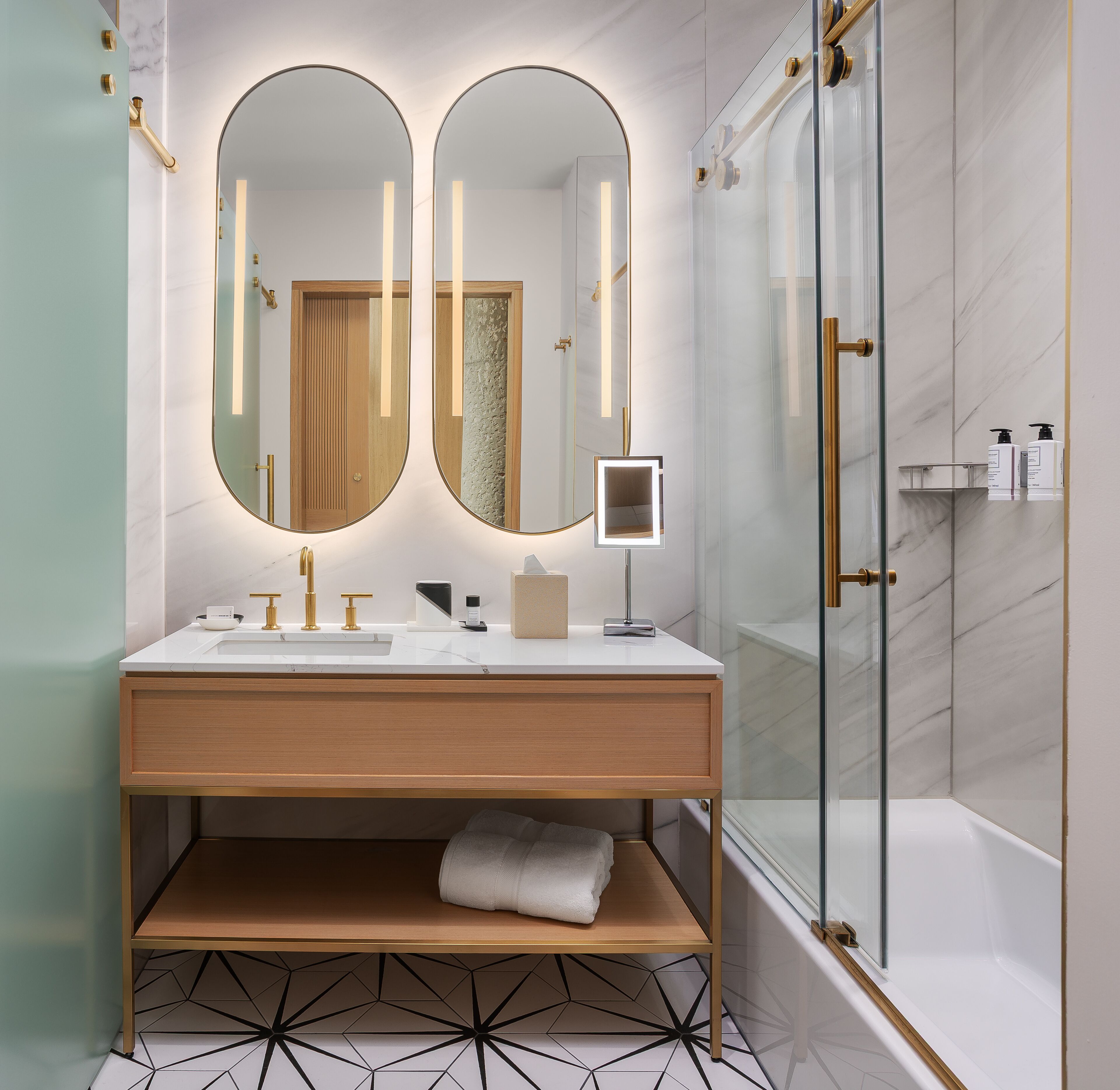 A modern bathroom with a double vanity, a glass shower enclosure, and a geometric patterned floor.