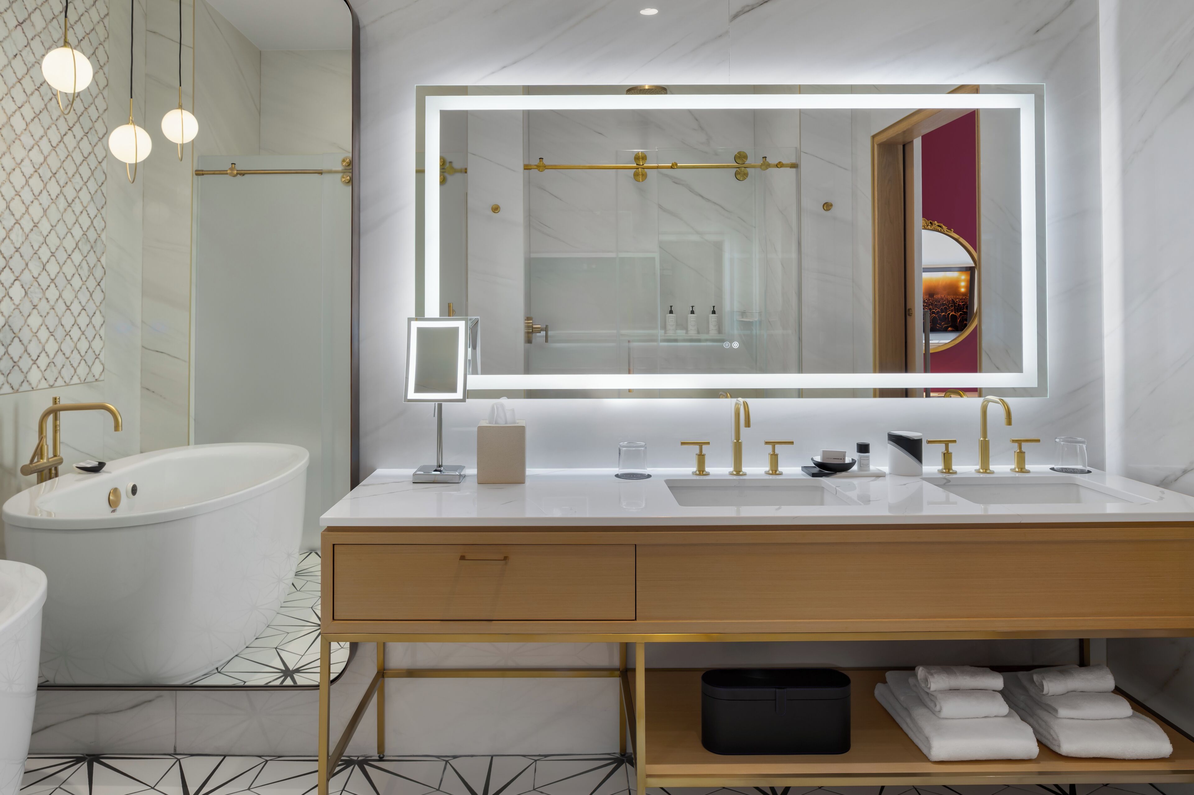A modern bathroom with a large mirror, dual sinks, a bathtub, and a vanity with storage.