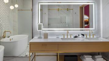 A modern bathroom with a large mirror, dual sinks, a bathtub, and a vanity with storage.