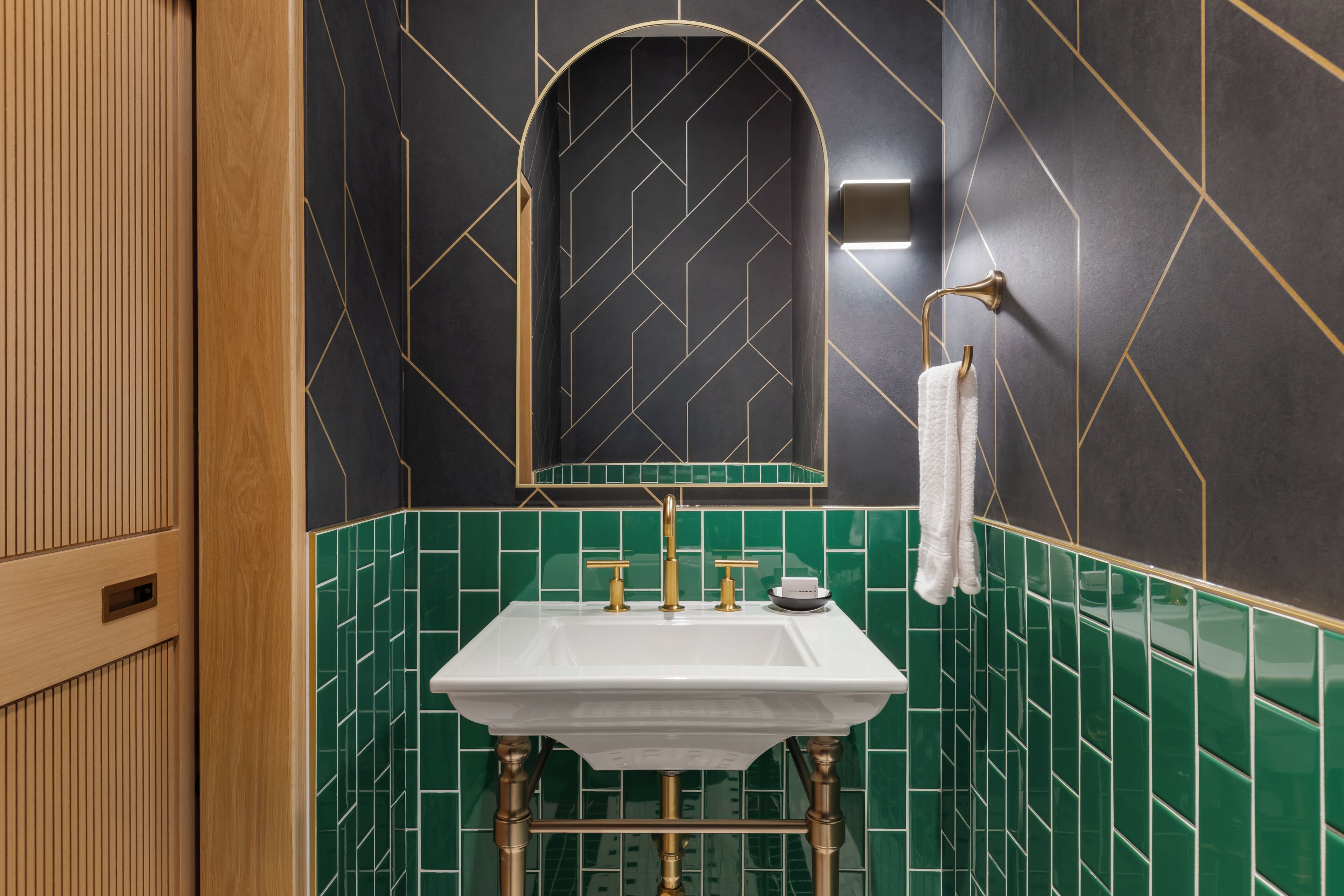 Un baño con un lavamanos blanco, grifos dorados y azulejos verdes.