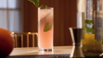 Un vaso alto con una bebida rosa, hojas de menta y cubitos de hielo.