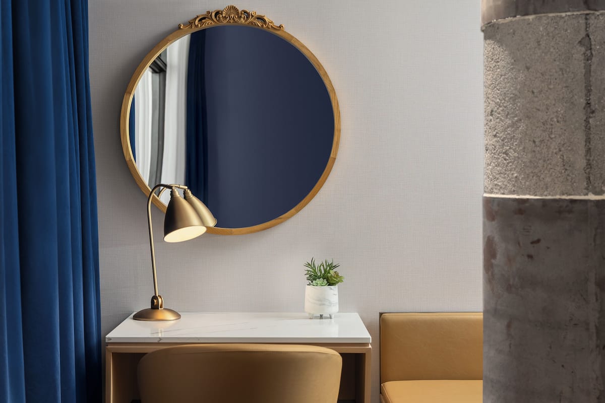 Une pièce avec un miroir rond, un bureau, une lampe, une petite plante et un canapé.