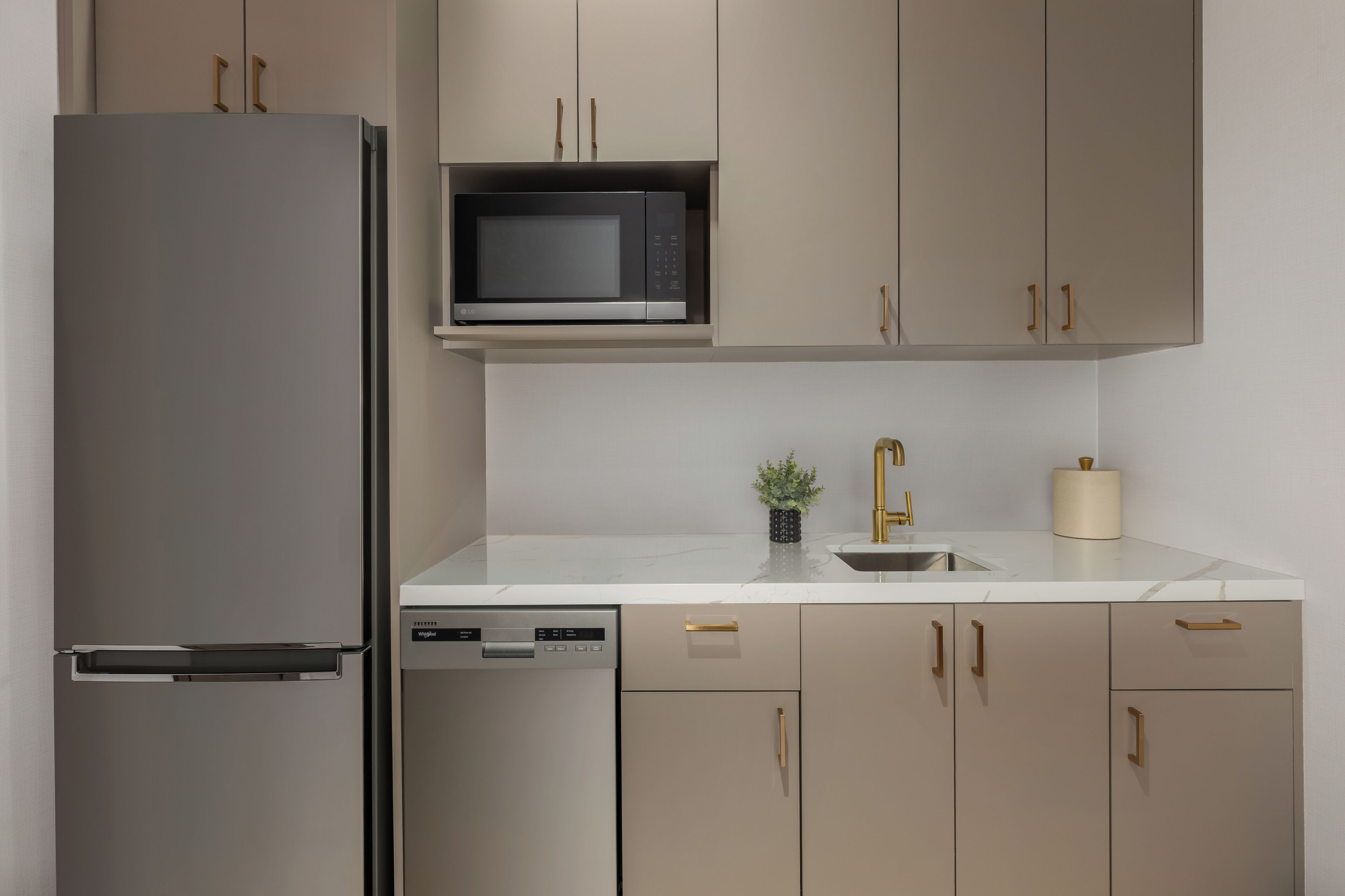 Uma cozinha equipada com frigorífico, micro-ondas, máquina de lavar loiça, pia e armários.