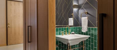 A bathroom with a wooden door, a sink with a gold faucet, and green tiled walls.