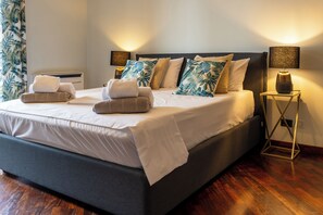 A neatly made bed with towels, a bedside table with a vase, and a wall-mounted lamp.