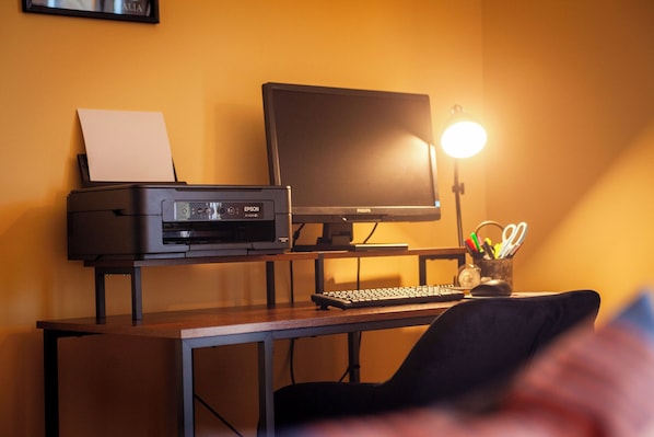 Un bureau avec une imprimante, un écran, un clavier et une lampe.