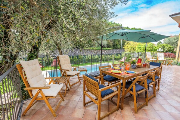 An outdoor patio with a pool, wooden furniture, and a green umbrella.