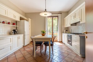 A modern kitchen with white cabinetry, a dining table with chairs, a hanging light fixture, and a view through a glass door.