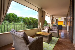 A balcony with wicker furniture, a tiled floor, and a view of greenery.