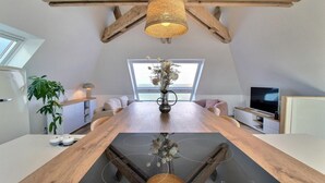 A modern loft-style room with a large wooden dining table, a hanging woven light fixture, a large window with a view, a flat-screen TV, and a built-in kitchen area. - Apartment residence Gulf Stream, Santec, Théven (Santec)