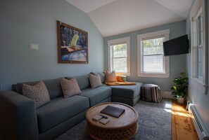 Un salon avec un canapé d’angle, une table basse ronde, un tableau et un téléviseur fixé au mur.